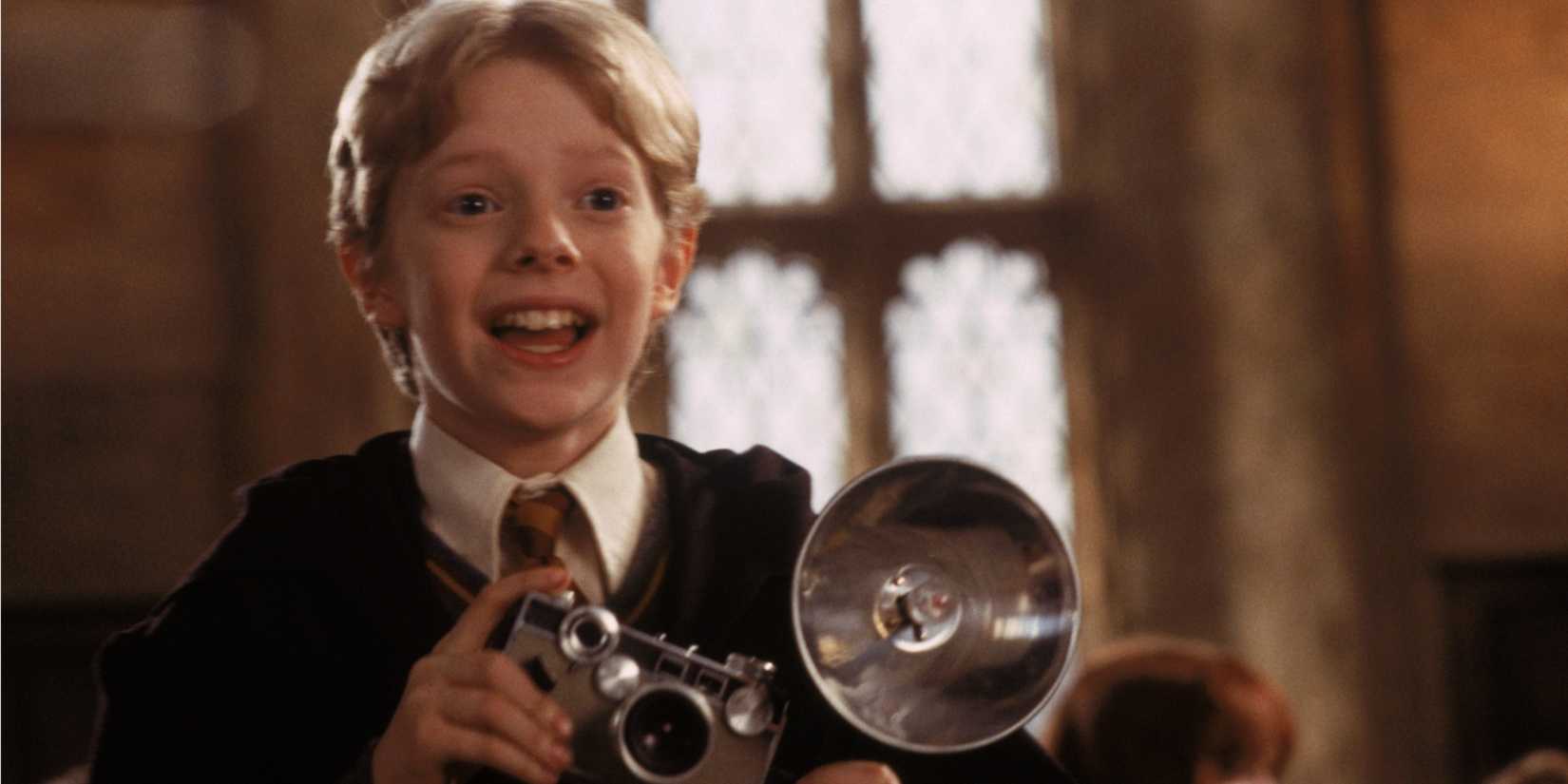 Colin Creevey (Hugh Mitchell) smiles and holds a camera in Harry Potter and the Chamber of Secrets.